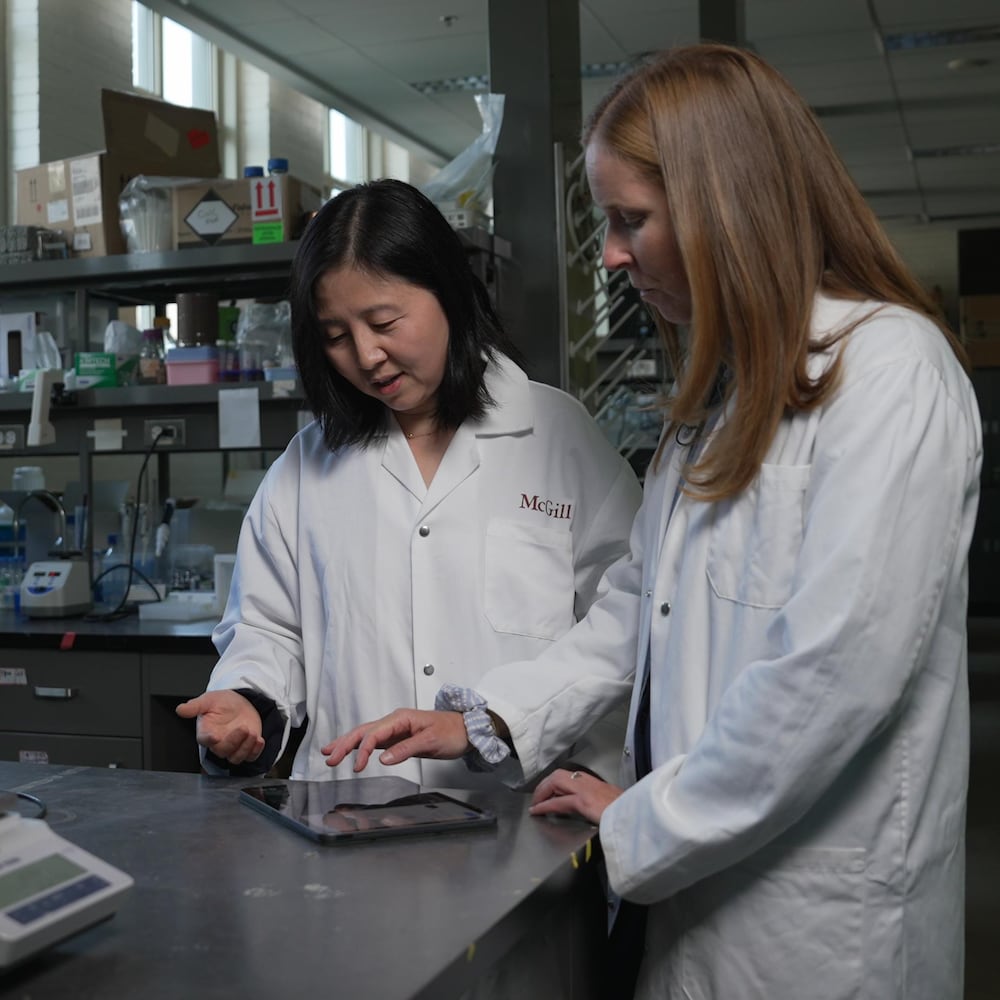 Deux femmes vêtues de sarraus blancs regardent des données sur une tablette électronique dans un laboratoire. 