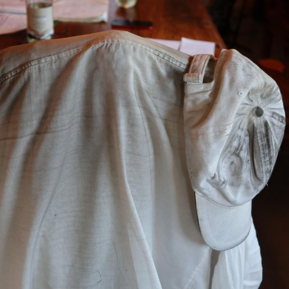 Une chemise et une casquette sales sont accrochées sur le dossier d’une chaise de cuisine.