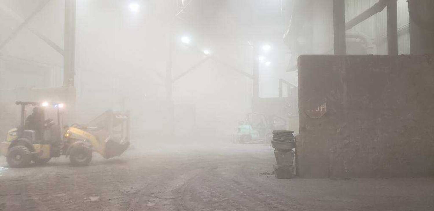 Another hazy picture of the containment room where a worker drives a loader through the dust.