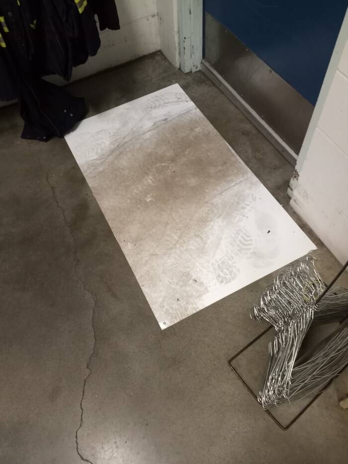 A white mat stained brown and covered in footprints sits on the floor of the employee locker room.