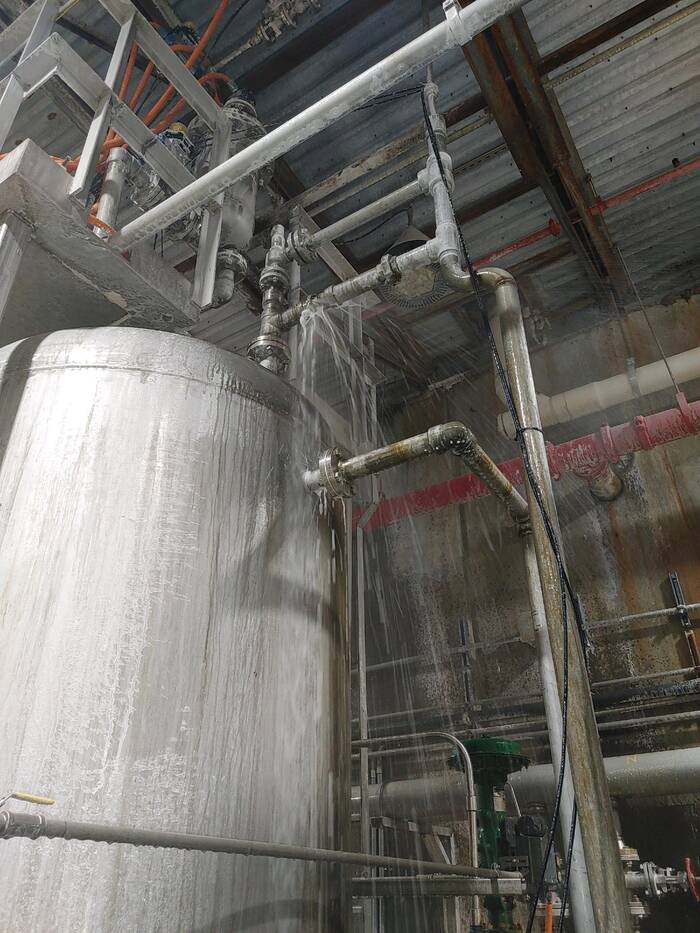 A white tank, covered in grey-brown dust and streaked by liquid pouring out of a pipe above the tank.