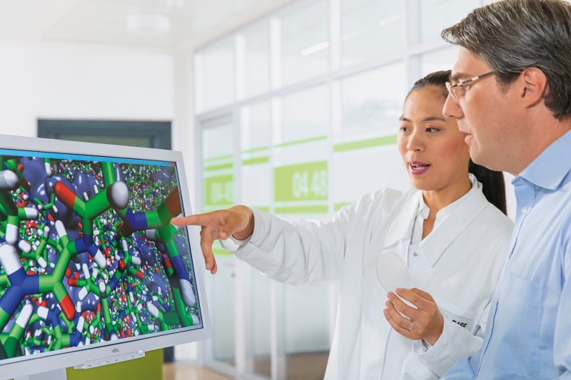 Two people gather around a computer monitor that has colorful molecular shapes displayed