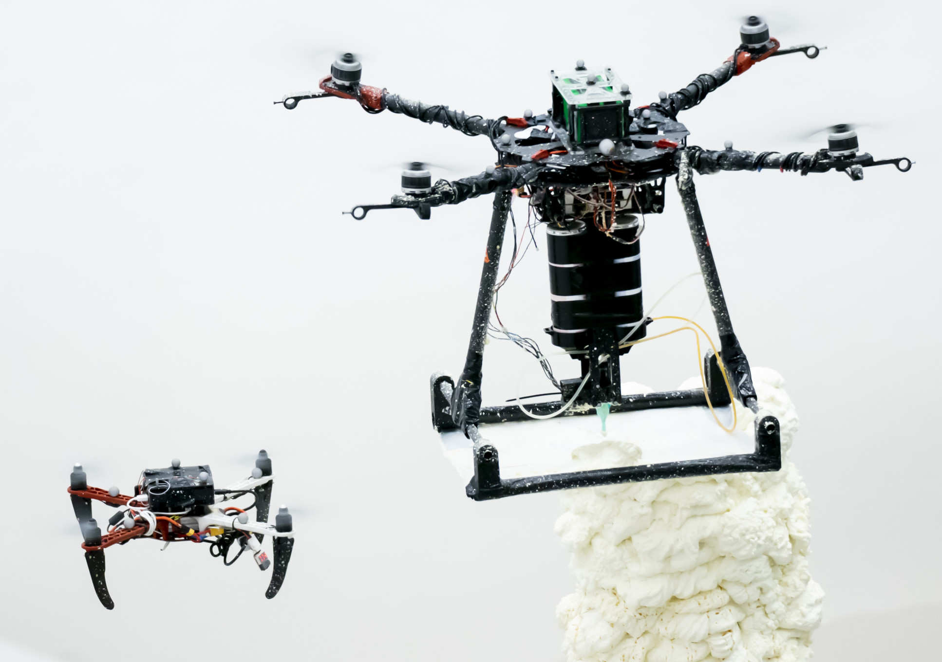 Smaller drone next to a larger drone which is printing a white material