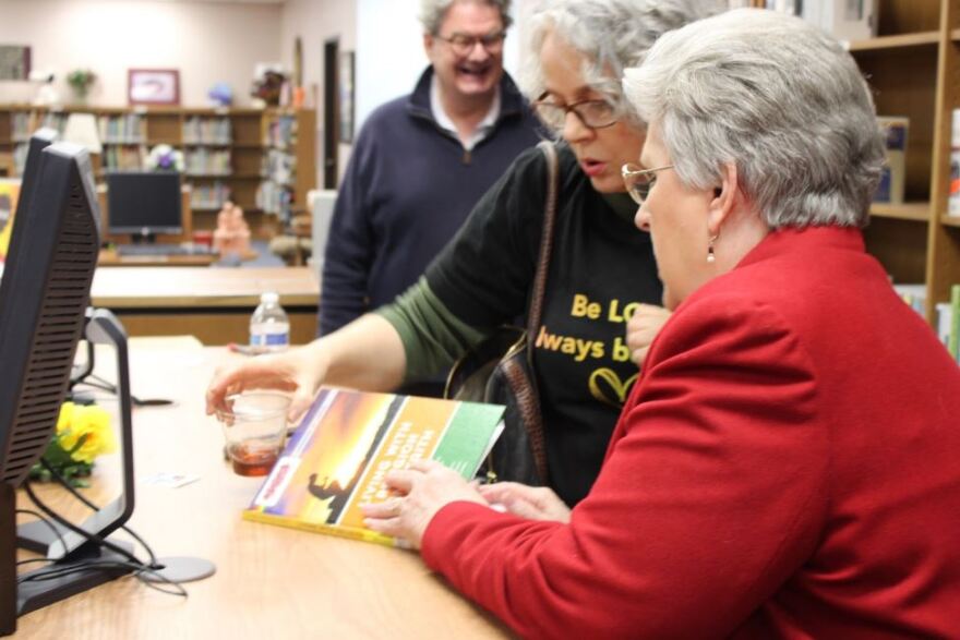 Lou Anne Mauldin, right, shows the book “Living With Religion and Faith” by Robert Rodi to church members during Broadway Baptist’s LGBTQ+ ribbon-cutting for its new shelf. Mauldin said she didn’t know that the book had been previously withdrawn from another library before she ordered it.