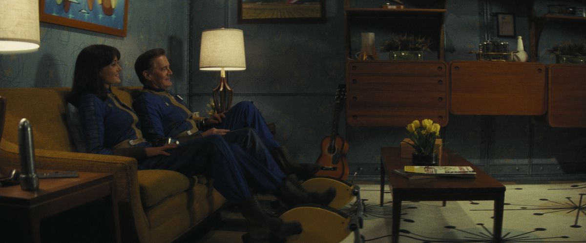 Lucy (Ella Purnell) and her dad Hank (Kyle MacLachlan) sitting on a couch smiling in a Vault living room