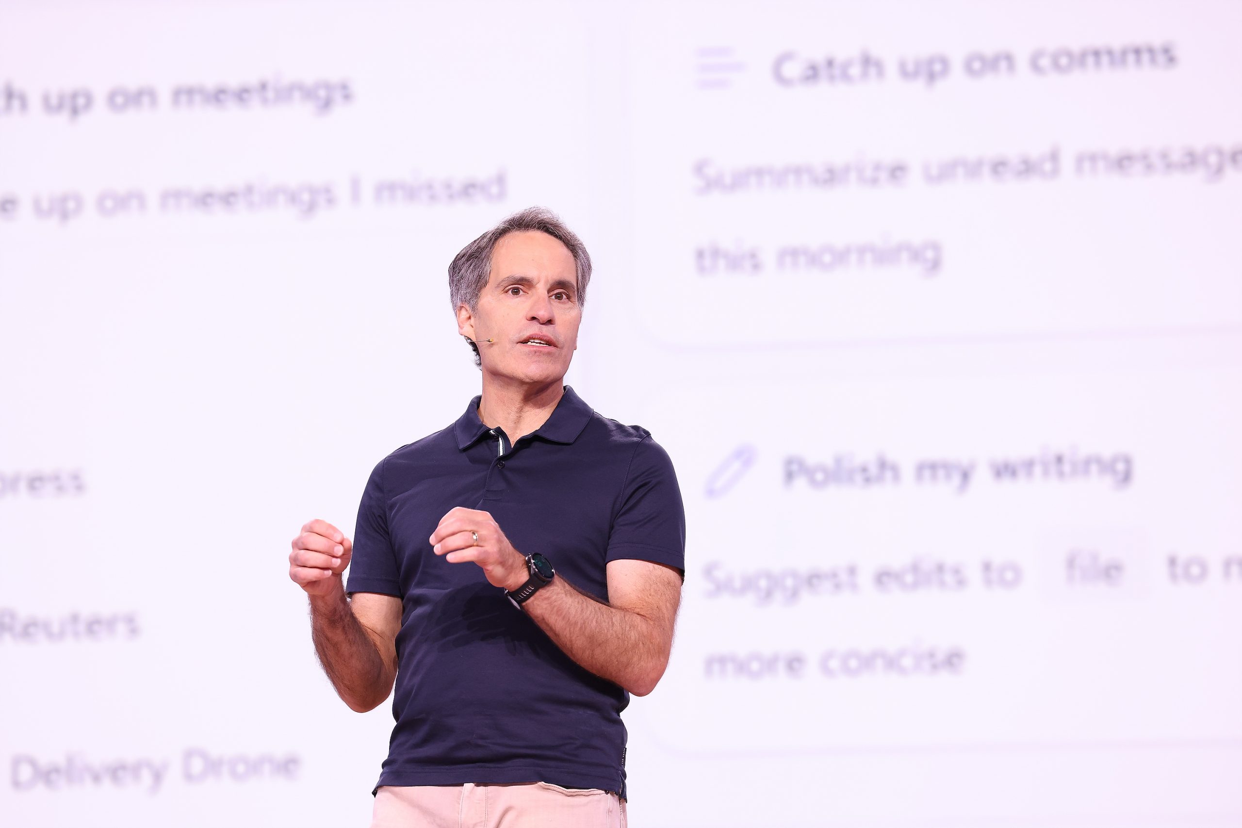 A man standing on stage with a light purple screen with dark purple text behind him