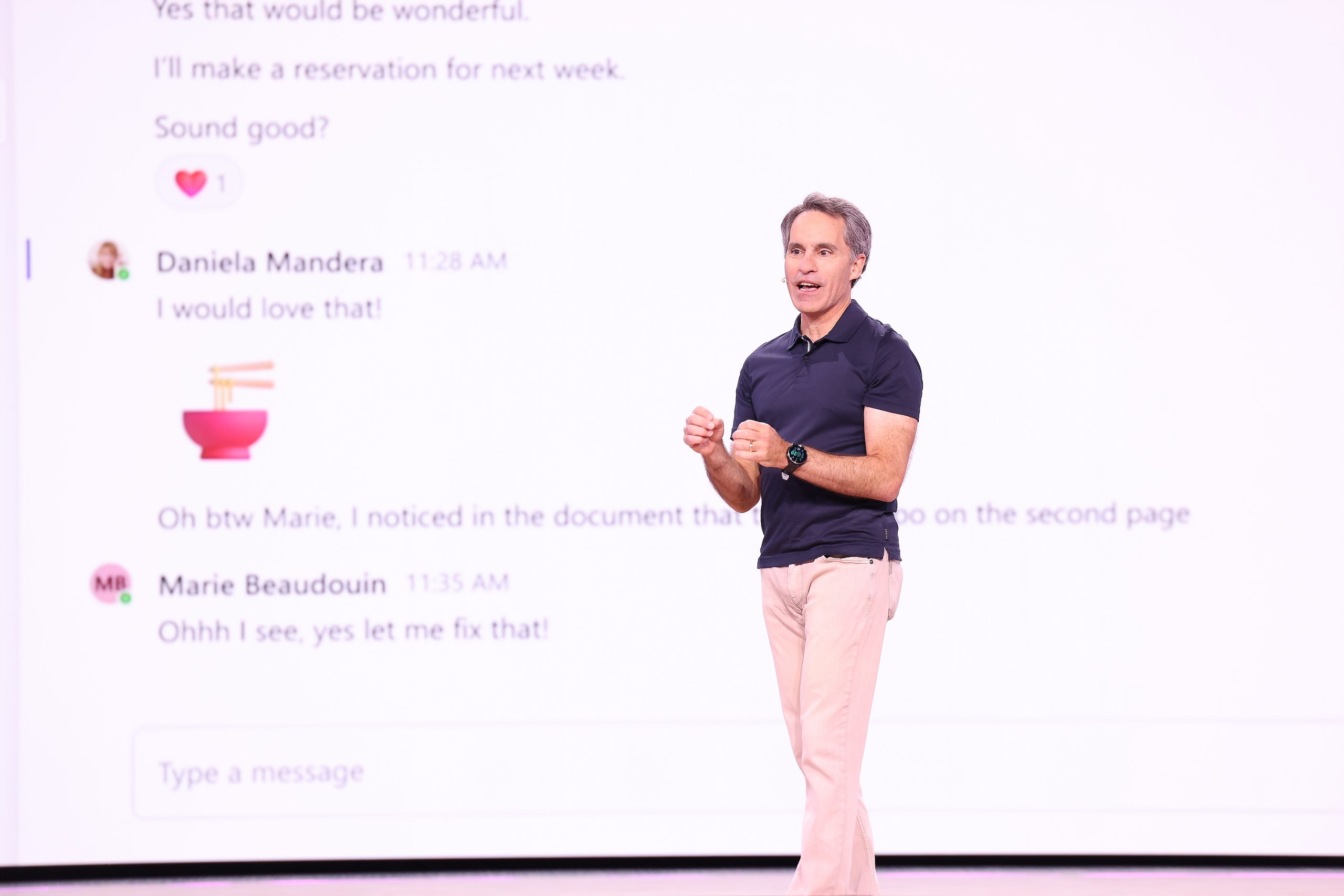 A man standing on stage talking to an audience with a screen behind him showing an active chat